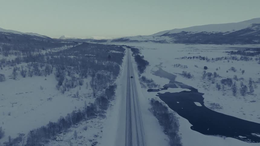 A car driving on an icy freeway in the countryside on a winter day with snow covering the surrounding area