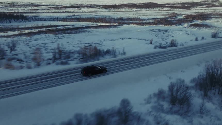 Van traveling on a snow covered rural highway with woodland across the landscape