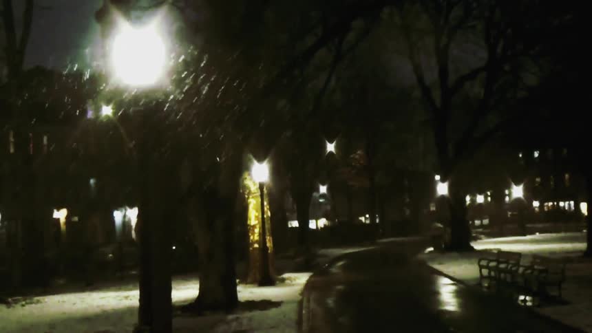 Snow falling onto the street at night with a streetlight illuminating the scene