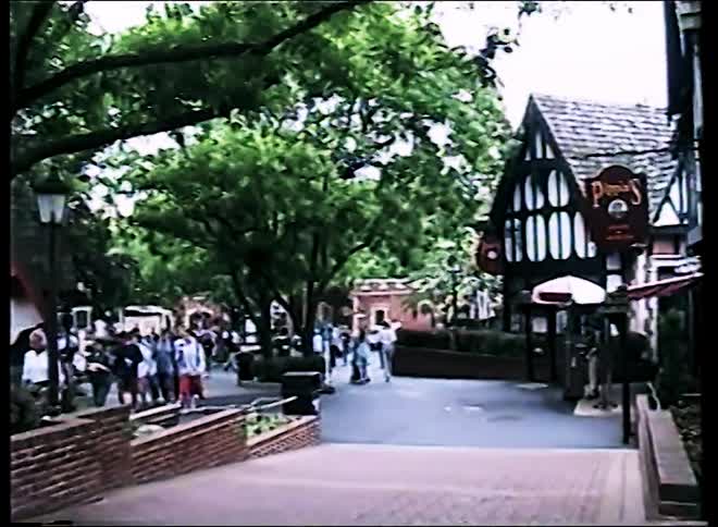 A busy street with people walking trees lining the center and buildings on either side