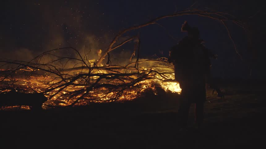 Person in traditional attire before nighttime bonfire