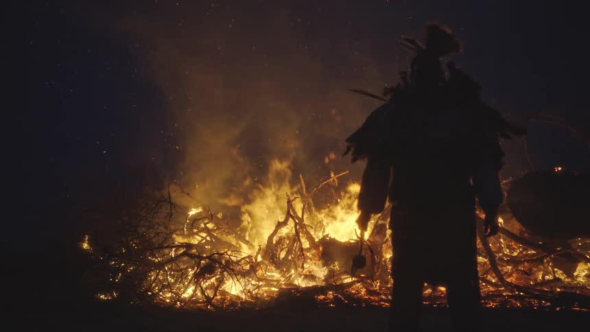A person standing outdoors at night in front of a fire
