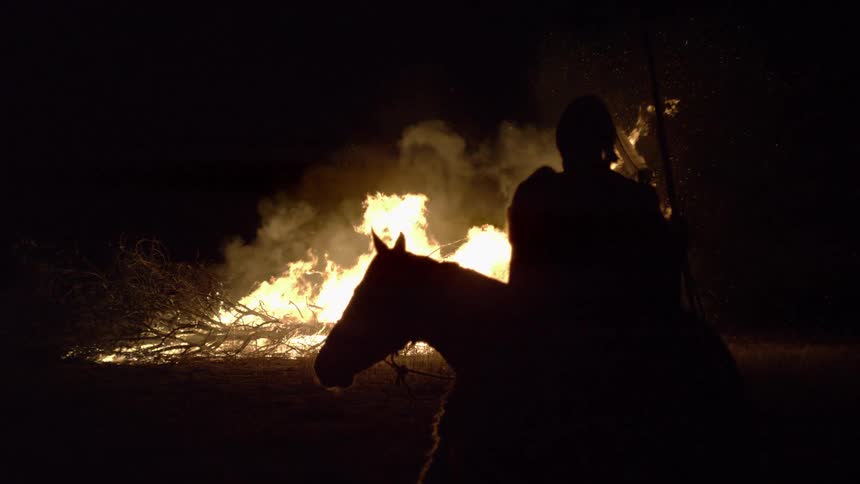 Silhouette of rider with spear before nighttime bonfire