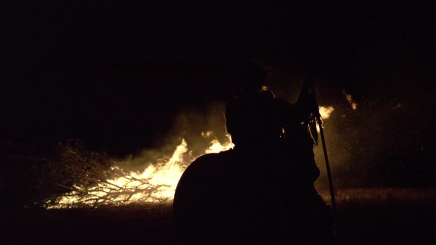 Silhouette of a person riding a horse in front of fire at night