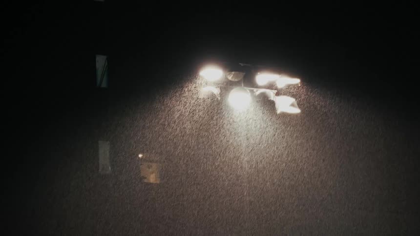 Bright stadium lights shine through heavy rain falling against a dark night sky at a sports field