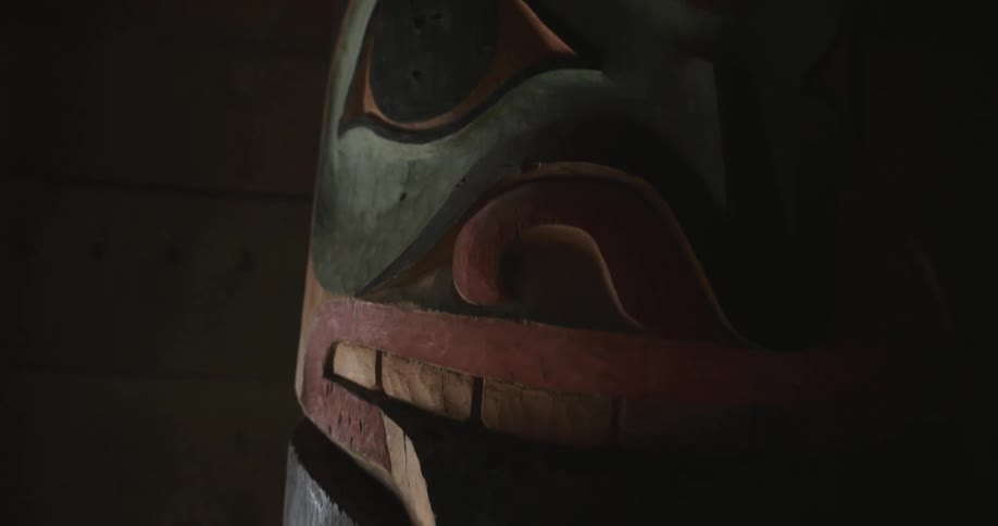 This video features extreme closeup shots of a handcarved totem pole highlighting the intricate details of its painted features and wooden texture the camera slowly pans across the sculpture in low light focusing on the stylized eyes and mouth chara