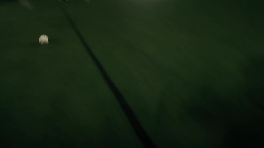A white soccer ball sits on a dark green artificial turf field with painted blue lines as a person kicks it