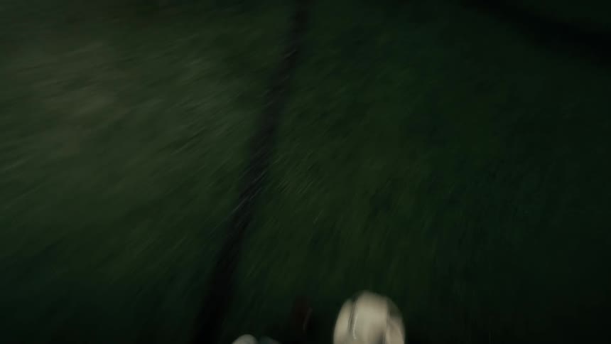 A soccer player in white cleats dribbles a classic patterned ball across a dark green artificial turf field
