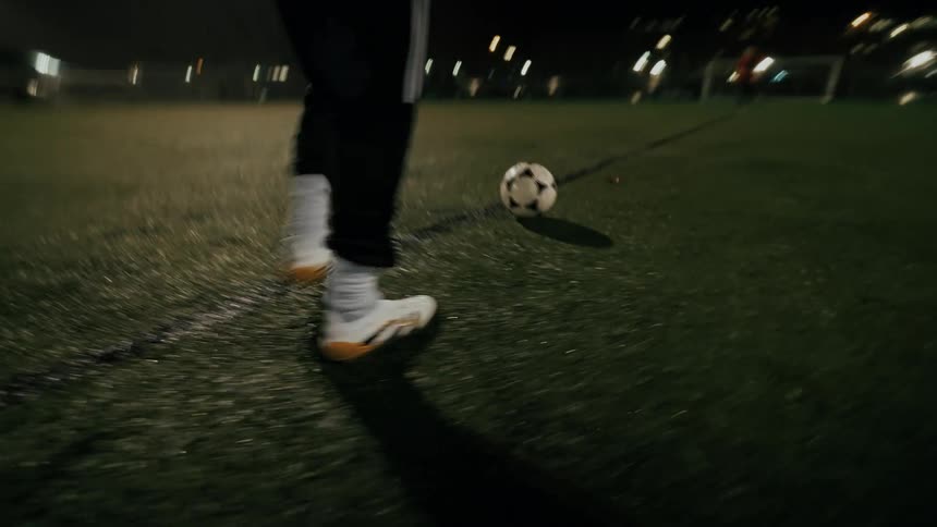 An athlete kicking a soccer ball across the field at night having fun