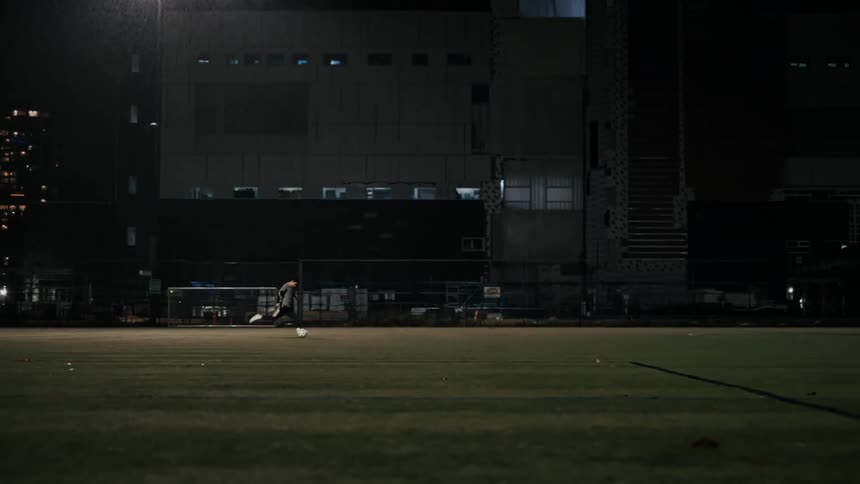 Player kicking a soccer ball towards the goal with the goalkeeper in a rainy night game