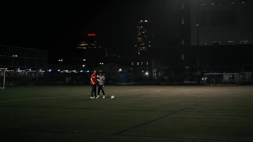 Two friends on an empty soccer field in the city at night bump fists