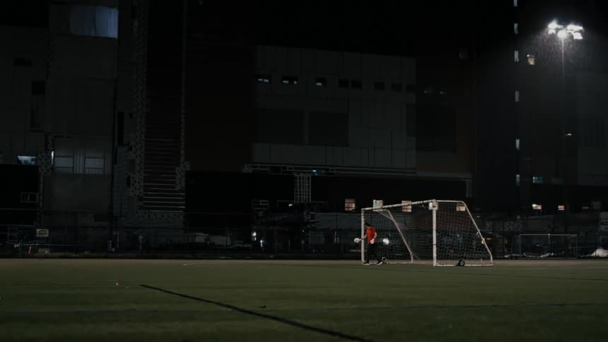 Goalkeeper kicking a soccer ball on an artificial turf field at night in the rain