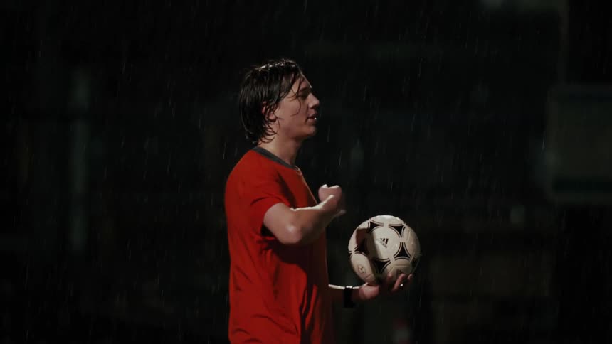 Man holds a soccer ball under rain at night