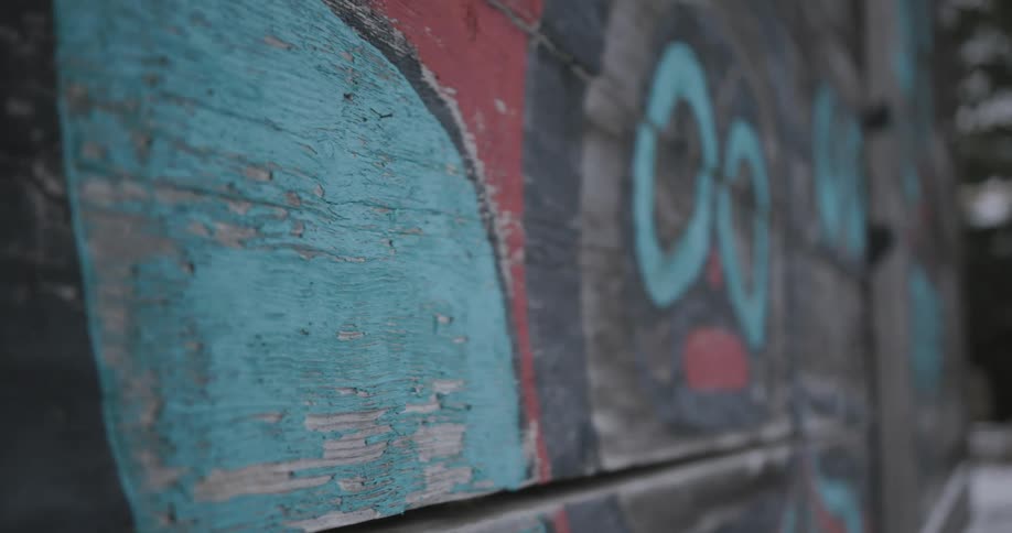 A closeup panning shot of weathered wooden planks adorned with faded colorful indigenousstyle artwork the peeling paint and rustic texture suggest the mural is part of an outdoor structure such as a longhouse or a large toteminspired wall