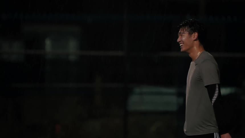 Man smiles under rain on a sports court at night