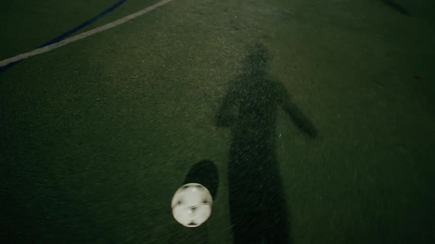 A person kicking a soccer ball across the field at night time