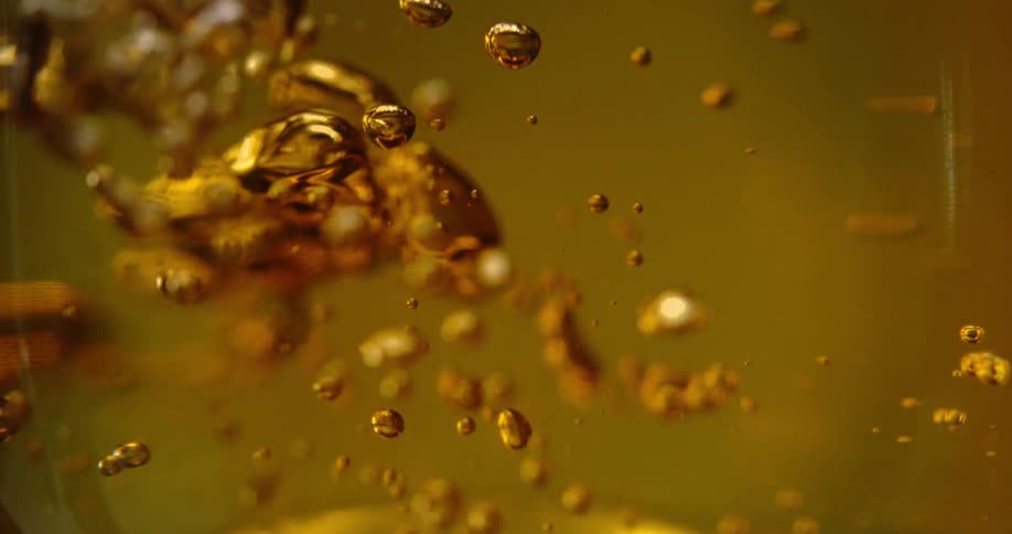 Golden liquid droplets suspended with splashes and bubbles against a yellow background