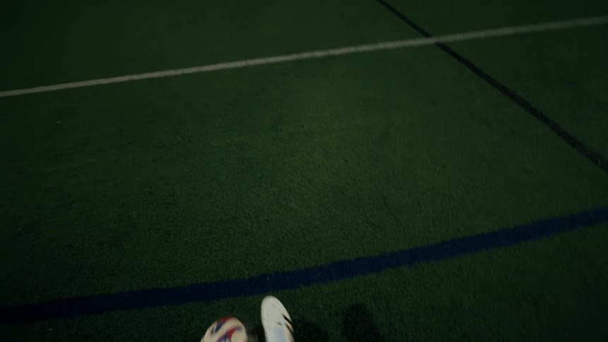 A person dribbles a soccer ball across a green turf field at night