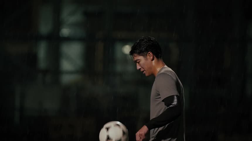 An athlete on a field at night juggling a soccer ball while drenched in sweat