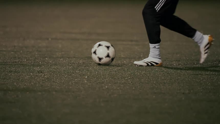 Two players feet battling for control of a soccer ball on a lit field at night