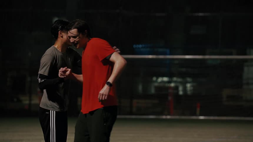 Two men greet each other on a sports court at night
