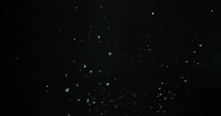Clear water droplets splash upward against a solid black background before falling back down in a slow motion view