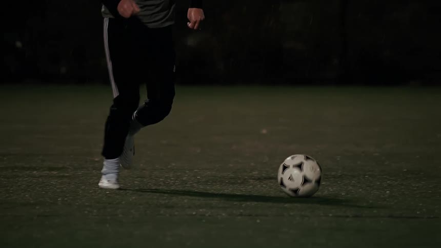 Player dribbling and kicking a soccer ball on a grass field at night