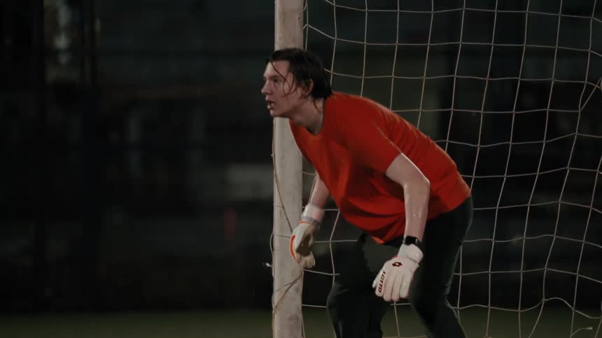 Goalkeeper tries to save ball near the goal net at night