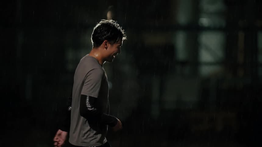 Man smiles under rain on a lit sports court at night