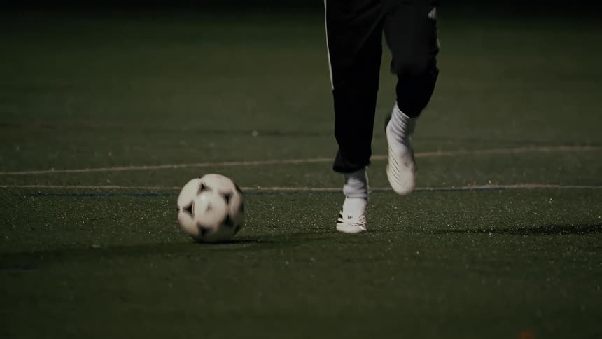 A person dribbling a soccer ball across a field under stadium lights at night