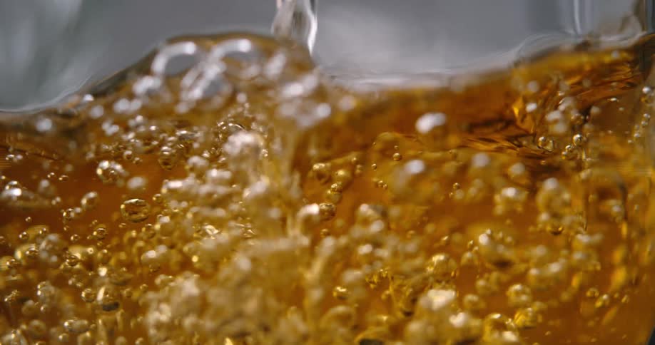 Golden liquid with effervescent bubbles and turbulent motion against a blurred background