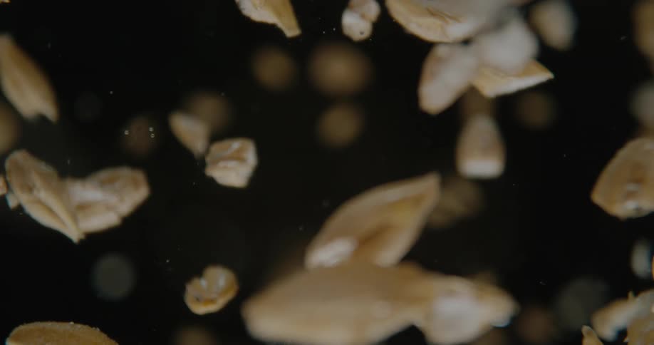 A close view shows many light brown grains falling and spinning against a black background