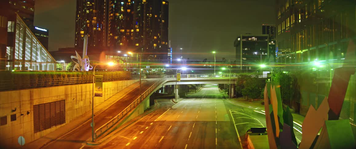 Empty urban avenue at night with illuminated buildings and overpass