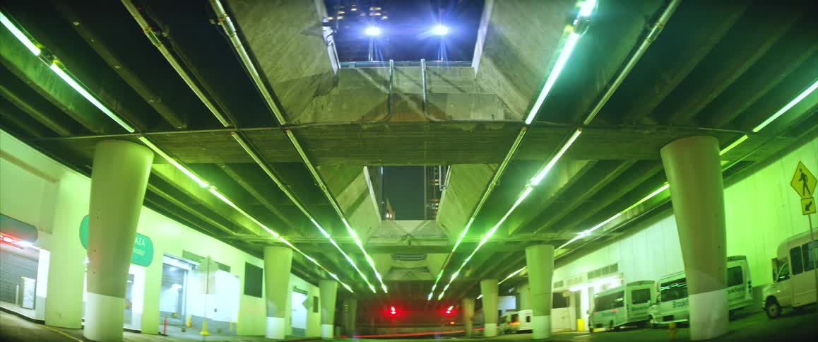 Urban roadway under an overpass with green lighting and red signal in the background