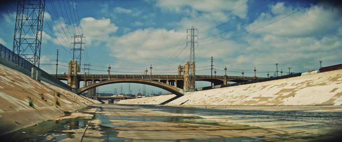 Concrete bridge crosses urban channel with power towers around