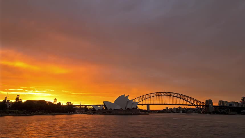 Sydney opera house and harbour bridge under an orange sky at dawn and dusk