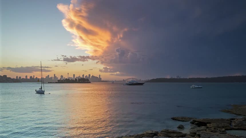 Boats sail in a bay at sunset with city skyline in the background