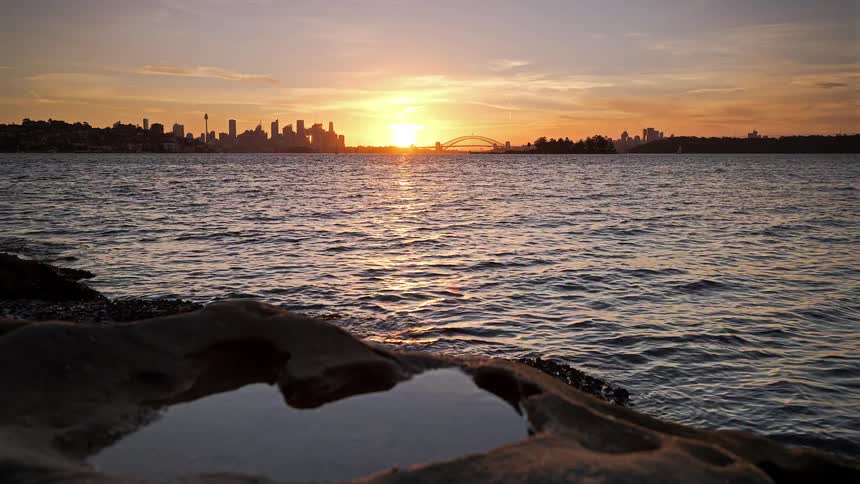 A rocky coastline with a city skyline in the distance at sunset