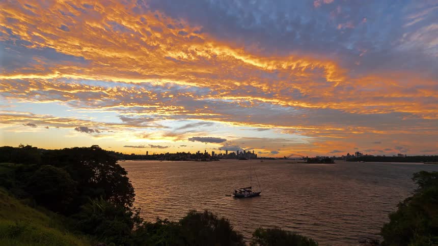Boats sailing on the water off the coast as the sun sets behind the metropolitan skyline in the distance