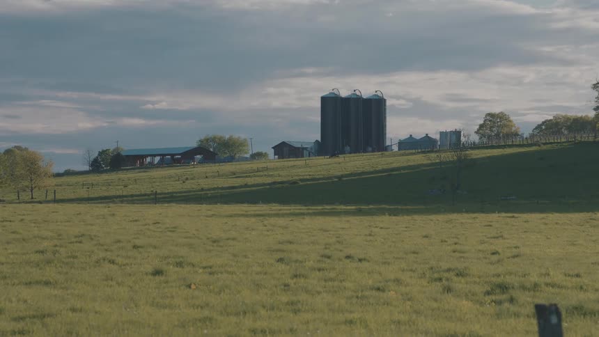 Silos and rural buildings on a hill surrounded by green field