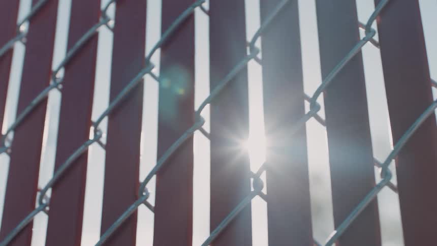 Sunlight shines brightly through a privacy chain fence at dusk