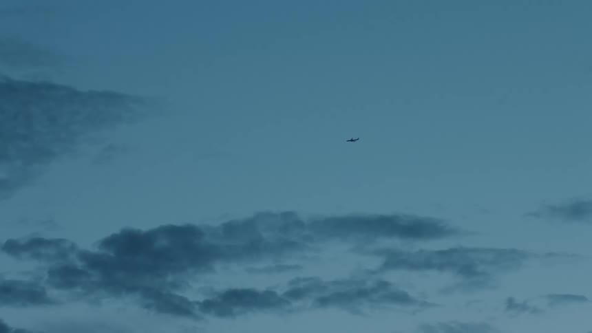 Airplane flies high in blue sky with scattered clouds