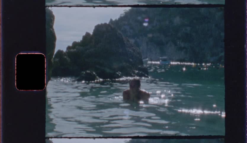 Person swims in the sea surrounded by rocks under natural light