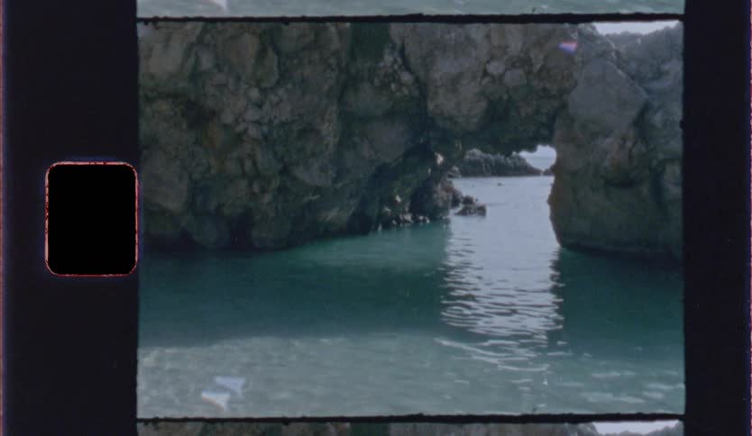 A natural stone archway over calm turquoise water nestled between rugged sea cliffs