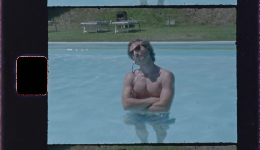 Shirtless man wearing sunglasses stands in an outdoor pool