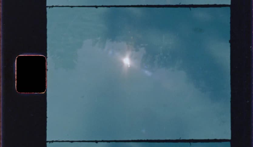 Vintage film footage shows a bright sun reflecting on the surface of blue water with visible film grain and dark borders containing sprocket holes