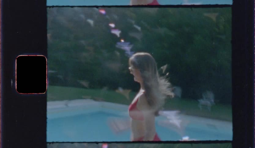 A woman in a red bikini walking past a swimming pool captured with a vintage film aesthetic the shot includes retro visual elements like film grain light leaks and a decorative sprocket hole border