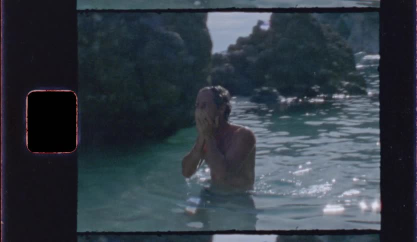 Man in the sea between rocks washes his face with water