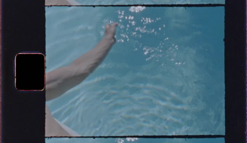 A persons arm reaches into clear blue water creating small ripples and splashes framed with a vintage filmstyle border