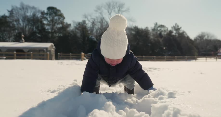 Child kneels in the snow and touches the ground with hands